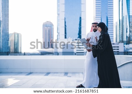 Arab couples or colleagues working together on tablet or laptop wearing traditional clothes and abaya. Muslim employees Saudi or Emirati business woman and man Royalty-Free Stock Photo #2161687851