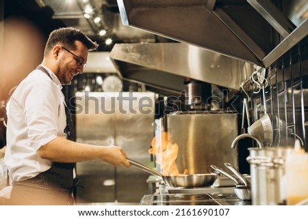 Man chef frying meat in a pan in fire