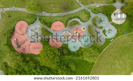 An aerial view directly above a children's playground in a park in Brooklyn, NY. It was shot on a cloudy day, the park is surrounded by green grass and trees.