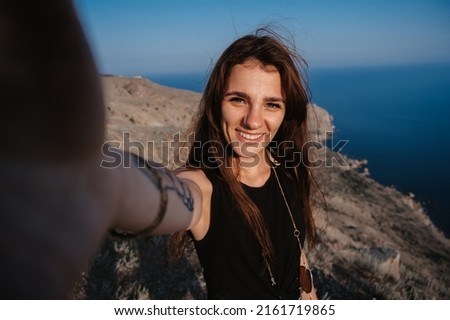Selfie-portrait of a young woman against the background of the sea at the cliff. The girl smiles at the camera. The concept of tourism, recreation