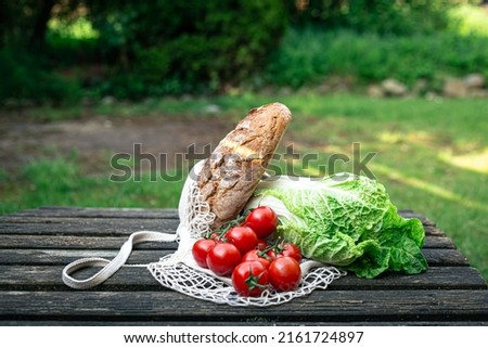 Vegetables and bread in a shopping bag on a wooden surface.