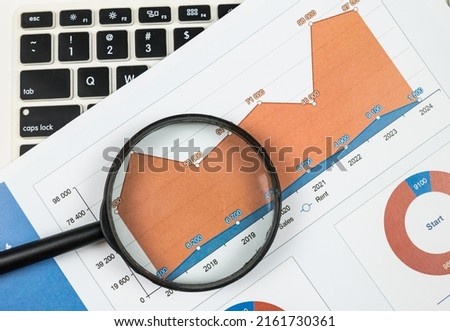 Top view of charts with magnifier and laptop. Spreadsheets, financial development graph, bank accounts, statistics, economics, data analysis, investment analysis, stock exchange