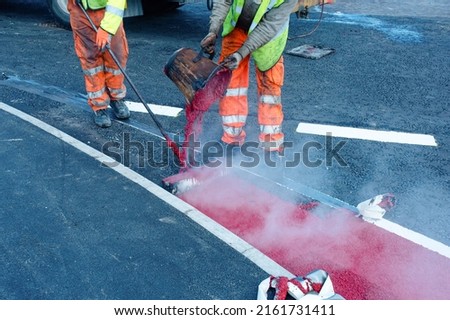 Road workers applying hot red road marking paint on new build road Royalty-Free Stock Photo #2161731411