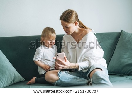 Young mother and cute baby girl using mobile phone at home