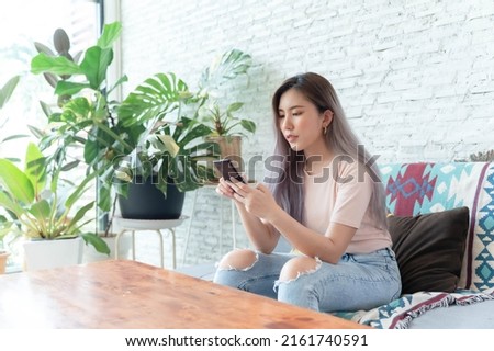 Asian woman sitting on her cell phone and smiling in her home photo.