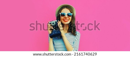 Summer portrait of happy smiling young woman photographer with vintage film camera on colorful pink background
