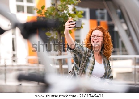 Beautiful smiling red hair student girl taking self portrait with a smartphone in front o a university building