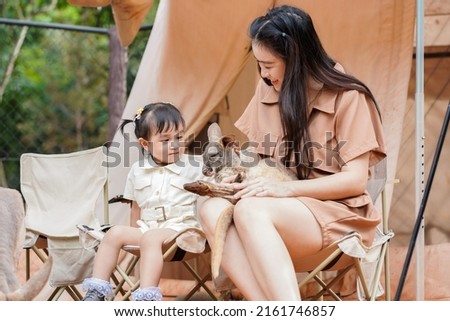 Asian cute little girl sitting and taking care of small kangaroo holding by her young mother in the zoo.