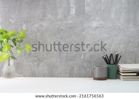 Stylish workplace with coffee cup, book, pencil holder and potted plant on white table against loft wall. Copy space for your text.