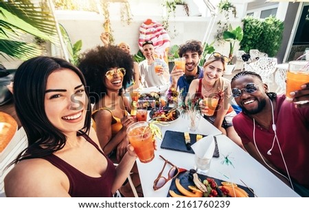 Multiracial group of friends enjoying meal having backyard dinner party - Young people toasting cocktail glasses together at bar restaurant - Social gathering concept with guys and girls taking selfie Royalty-Free Stock Photo #2161760239