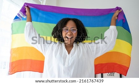 African American young woman smiling and raising and waving the LGBT flag in the air in bedroom.LGBTQ Sextual equality,Homosexual,Lesbian pride month,festival celebration concept.