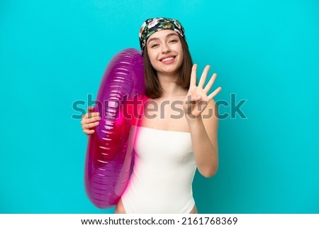 Young Ukrainian woman holding air mattress isolated on blue background happy and counting four with fingers