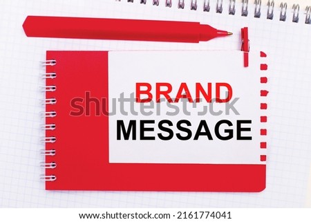 On a white notepad, a red pen, a red notepad and a white sheet of paper with the text BRAND MESSAGE