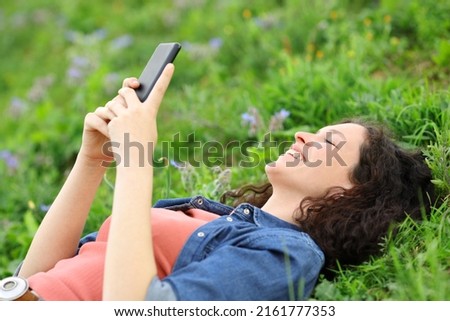 Happy woman lying on the grass using smart phone in a park