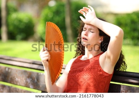 Woman in a park suffering heat stroke fanning Royalty-Free Stock Photo #2161778043