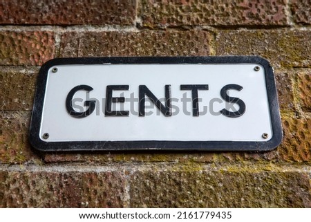 Close-up of a GENTS sign on a brick wall.