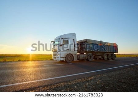 Semi-truck with tipping cargo trailer transporting sand from quarry driving on highway hauling goods in evening. Delivery transportation and logistics concept Royalty-Free Stock Photo #2161783323