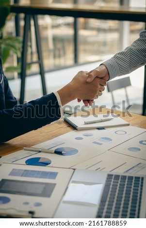 businesspeople shaking hands after the meeting Confident business team shakes hands during office meeting Success, Contact, Greeting and Partner concepts with graph documents and laptop on the desk.