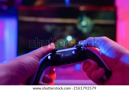 Gamepad in the hands of a gamer on a technological background. Plays online video games with friends. Fun pastime, adventure games, youth culture. Close-up.