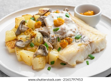 Close up view of fried cod fillet served with baked potato and grilled mushrooms, yellow berries and cloudberry sauce. Delicious food. Hot dinner or lunch. White background.