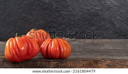 Three Raf Coeur De Boeuf tomatoes on a wooden background, rustic concept, space for text, stock photo
