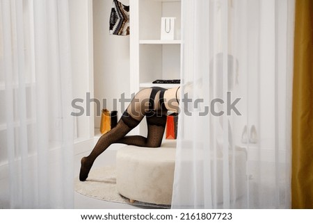 Unidentified young woman in tights leaned on her knee and her hands on the pouf in dressing room