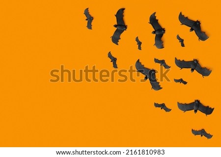 A lot of black bats flying on an orange background. Scary halloween flat lay composition on an orange background. Halloween decoration concept.