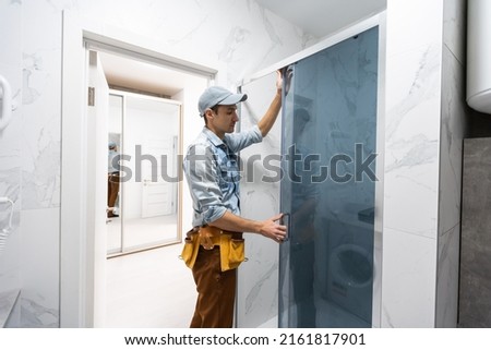 Handyman installing glass cabinet in bathroom. Royalty-Free Stock Photo #2161817901