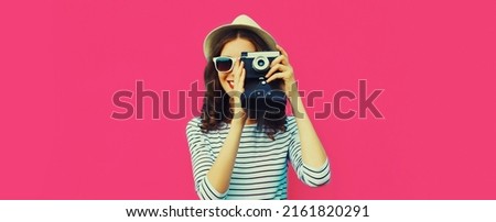 Summer portrait of happy smiling young woman photographer with vintage film camera on colorful pink background