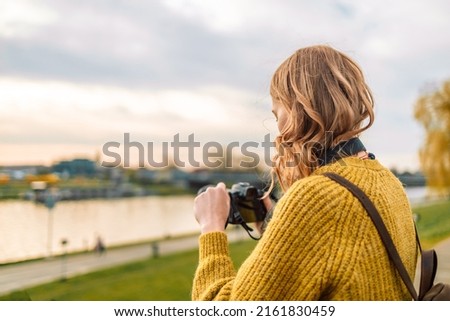 Caucasian girl taking photo outdoors with digital camera. young blonde girl photographer adjusts the camera to take a photo of the city, banner.