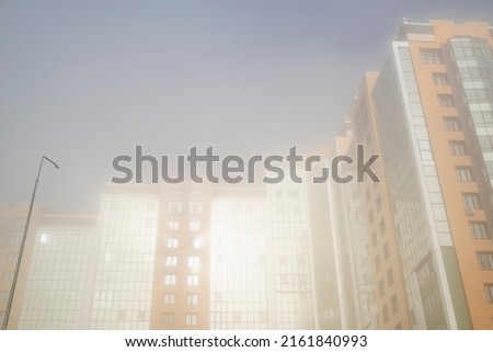 Multi storey residential buildings in the morning fog and the rays of the dawn sun.