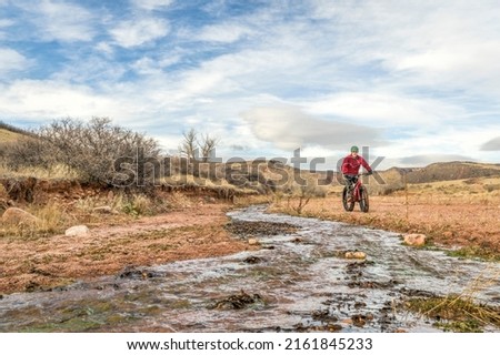 male cyclist is riding a fat mountain bike along a stream in Red Mountain Open Space, Colorado , late fall scenery