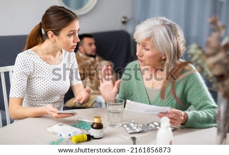 Women arguing about treatment of ill man at home. Senior woman reading instruction for medicine, her daughter-in-law searching information in internet with smartphone. Royalty-Free Stock Photo #2161856873