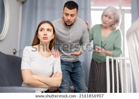 Depressed young woman ignoring her husband and mother quarreling with her in apartment. Royalty-Free Stock Photo #2161856907