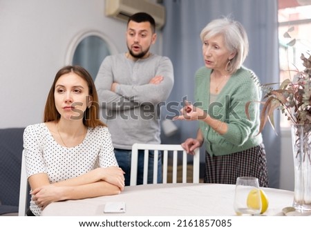Woman ignoring her husband and mother-in-law standing behind and arguing with her at home. Royalty-Free Stock Photo #2161857085