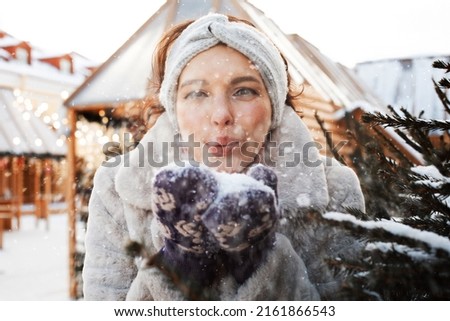 Lovely young woman in winter clothes plays with snowflakes next to the Christmas tree, winter, christmas market.