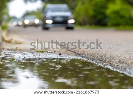 A puddle next to a busy road with cars driving by after a rain storm Royalty-Free Stock Photo #2161867973