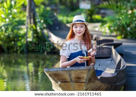 Young Asian woman tourist is travel with wooden boat in floating market in Thailand and having local street food for Southeast Asia tourism Royalty-Free Stock Photo #2161911465