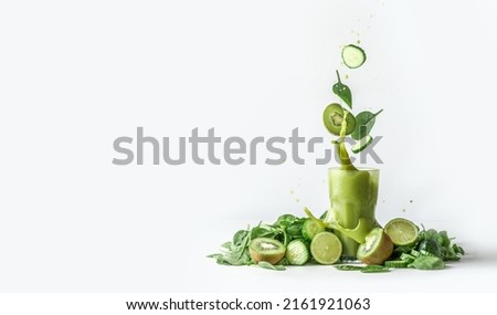 Green smoothie splashing in glass and flying ingredients: cucumber,kiwi and spinach leaves at white background with heap of green fruit and vegetable. Border. Front view. Royalty-Free Stock Photo #2161921063