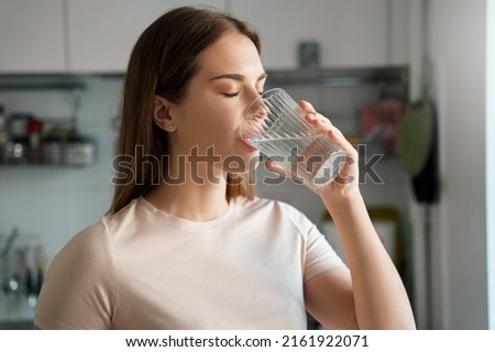 Thirsty young woman drinking fresh water from glass. Home office kitchen interior. Headshot portrait. Dehydration prevention, normal bowel function and balance of body maintenance concept Royalty-Free Stock Photo #2161922071