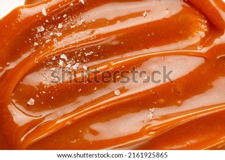 Liquid salted caramel syrup. Background of salted caramel paste. Texture Close up, top view. Sea salt pieces on caramel. Royalty-Free Stock Photo #2161925865