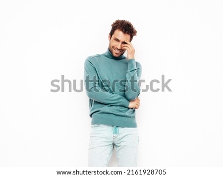 Handsome smiling hipster  model.Sexy unshaven man dressed in summer stylish blue sweater and jeans clothes. Fashion male with curly hairstyle posing in studio. Isolated on white Royalty-Free Stock Photo #2161928705
