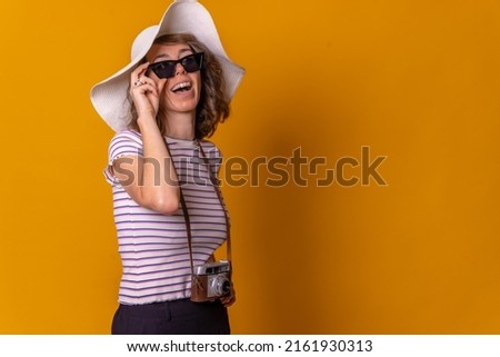 Caucasian girl in tourist concept smiling with a hat and sunglasses enjoying summer vacation, yellow background