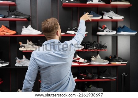 young man picking a sporty shoes in the shop, new sneakers in sports store for men, mens shopping sports shoes Royalty-Free Stock Photo #2161938697