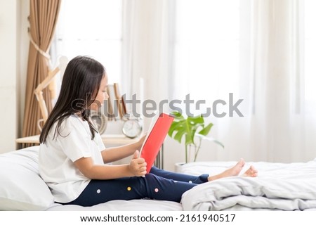 Asian child little girl read a book on the bed at home.