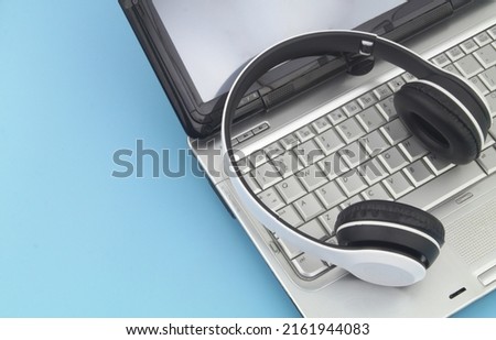 Wireless headphones with silver laptop computer on blue background. Copy space for text.