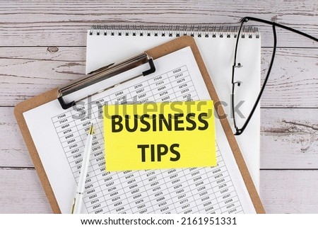 BUSINESS TIPS text on a yellow sticky on clipboard with chart, wooden background