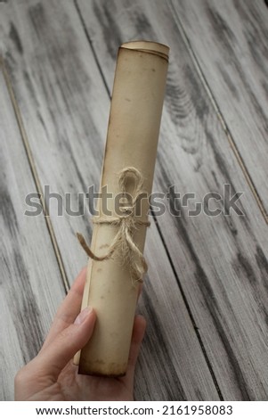 Woman holds in her hand an ancient rough scroll against a wooden surface.