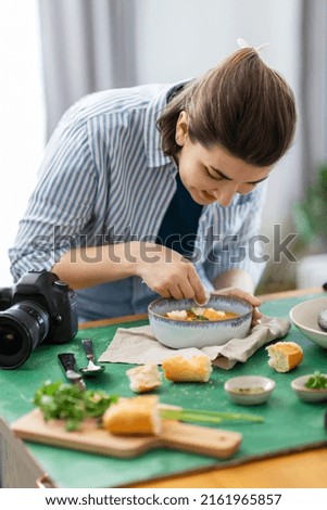 blogging, photographing and people concept - happy smiling female food photographer with camera arranging composition in kitchen at home