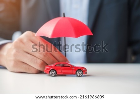 Businessman hand holding umbrella and cover  red car toy on table. Car insurance, warranty, repair, Financial, banking and money concept